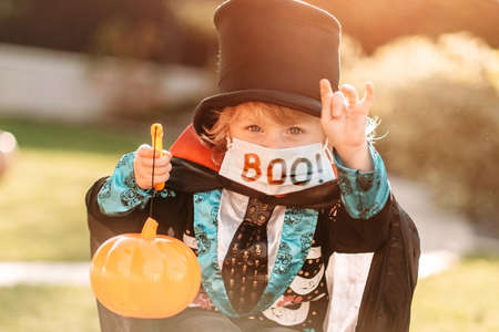 Happy Halloween. A child in a medical mask in a dracula costume sits on a pumpkin in his yard.