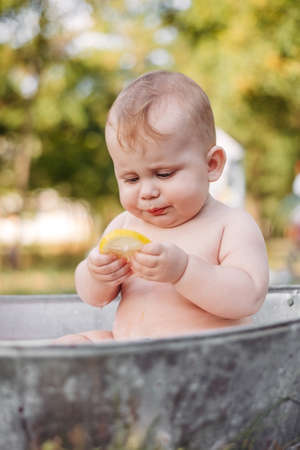 Cute baby in old fashioned metal bathtub playing with lemon piece in parkの写真素材