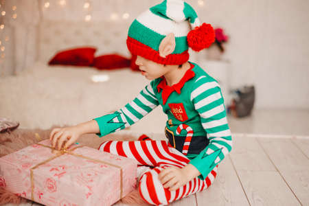 Happy boy dressed as a gnome sitting on the floor in his living room during Christmas time. Child holds a Christmas present.の写真素材