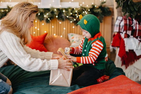 Mother makes a gift to her son. Mother with her lovely son on the background of the Christmas tree. Christmas at home. Traditionsの写真素材