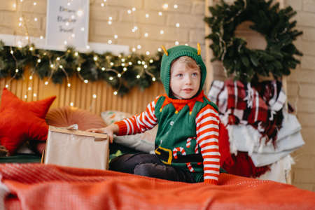 Happy new year concept. A happy blonde child sits on the bed and opens a box with a gift, a bright light shines on his face from the box, the child smiles happily and is pleased with the gift.の写真素材