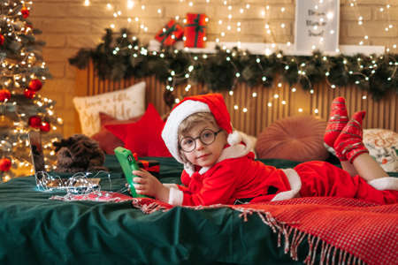 Cute boy in Santa Claus costume watching Christmas cartoons on tablet, preparing for celebration, wonderful atmosphere and decorations, miracleの写真素材