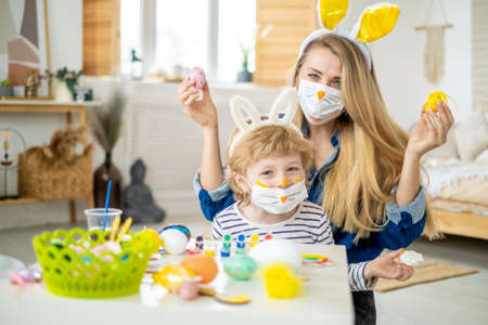 A masked family has fun on an Easter egg hunt during the coronavirus outbreak. Mother and son wearing bunny ears and bunny costumes in celebration of the coronavirus pandemic. Happy holiday.の写真素材