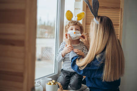 Masked family having fun during the coronavirus outbreak. Mother and son wearing bunny ears and...