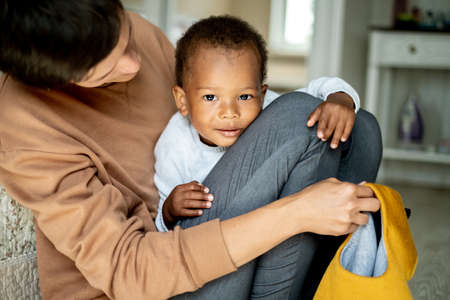 Caring caucasian woman hugging pretty African American baby boy, mother playing with her little son on the floor, family, adoption programの写真素材