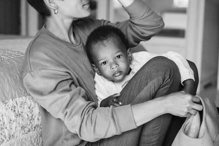 Caring caucasian woman hugging pretty African American baby boy, mother playing with her little son on the floor, family, adoption programの写真素材
