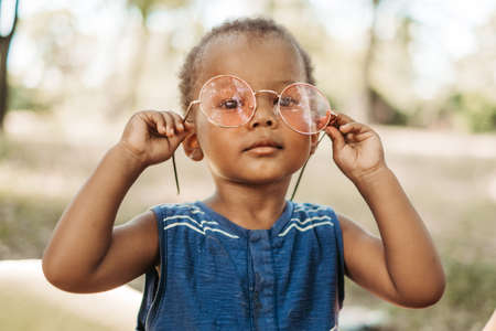 adorable african boy in trendy round pink sunglasses in the parkの写真素材