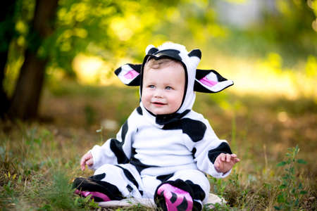 Year of the bull. A child in a fancy dress of a bull on a meadow smiles cute. Kid in Halloween Cow Costumeの写真素材