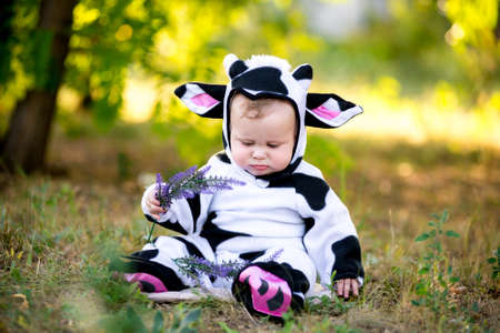 Year of the bull. A child in a fancy dress of a bull on a meadow smiles cute. Kid in Halloween Cow Costumeの写真素材