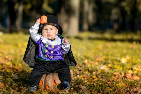 Cute baby boy in vampire costume sitting on pumpkin in autumn forest, halloweenの写真素材