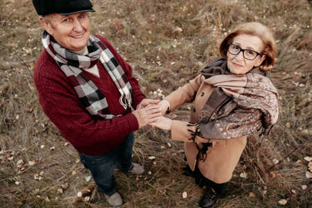 Senior man in love holding and caressing tender hands of his beautiful woman, husband warming cold wrinkled arms of wife during walk along park, couple confessing in love and fidelity, close-upの写真素材