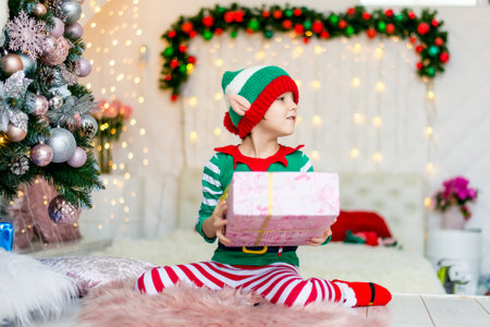 Happy boy dressed as a gnome sitting on the floor in his living room during Christmas time. Child...