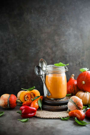 Pumpkin soup in a transparent jar on a table with autumn vegetables. Harvest tomatoes, pumpkins and peppers.の写真素材