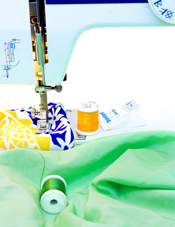 A foot of a sewing machine and a couple of rolls of tread with colorful cloth