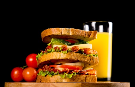 big sandwich with fresh vegetables on wooden board on black background
