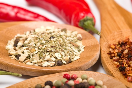 lot of spices in wooden spoons and chili peppers on white background