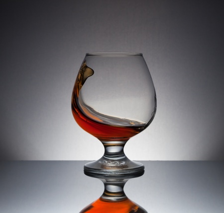 splashing cognac in glass with reflectionの写真素材