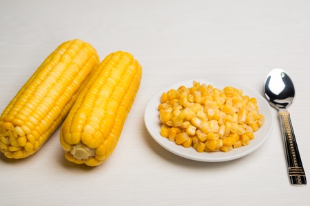 Heap of sweet yellow corn seeds, spoon and two cobsの写真素材