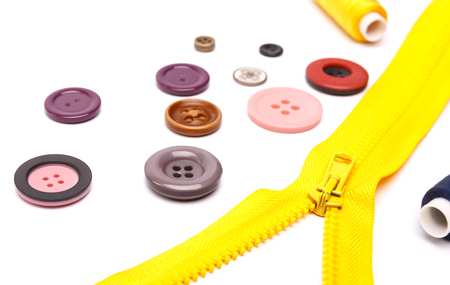 colorful rainbow reel of thread, a variety of buttons and yellow zipper on a white backgroundの写真素材