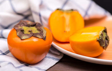 two persimmons on a plate and on a lienen towel on a wooden tableの写真素材
