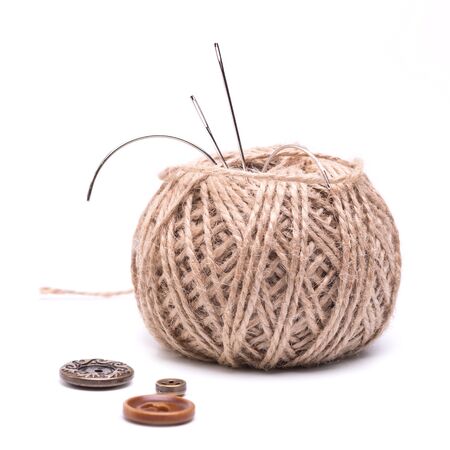 a needle stuck into the skein of  brown thread and a few buttons on a white backgroundの写真素材