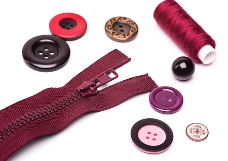 maroon zipper, coil colored threads and buttons in different shapes and sizes on a white backgroundの写真素材