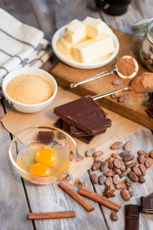 raw eggs, cocoa beans and powder, pieces of chocolate and spices on the wooden tableの写真素材