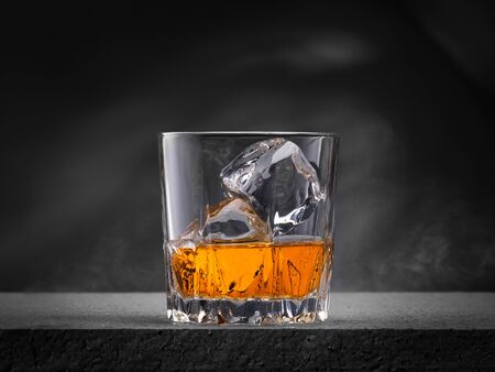 Glass of whiskey with ice cubes on the concrete table with gray backgroundの写真素材