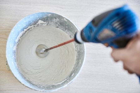 Worker mixing plaster in a bucket for alignment and putty walls of the apartment using an electric drill, close-up.の写真素材