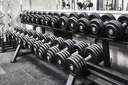 Rows of metal heavy dumbbells on rack in the sport gym, monochrome color tone. Sports equipment for...