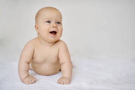 Cute baby in diaper on white background is lying on his stomach leaning on his hands, smiling and looking awayの写真素材