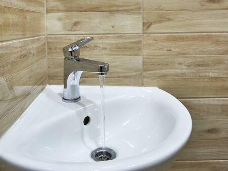 Modern water tap in the bathroom with running flowing water in sink. Open chrome sink faucet. Modern design bathroom.の写真素材