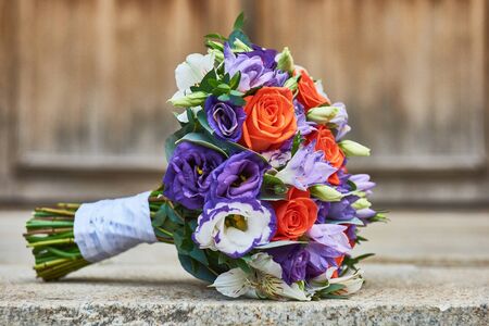 Wedding bouquet close-up of purple lilac irises, red scarlet roses and other flowers on the floor at wooden doorの写真素材
