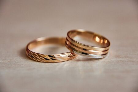 Two gold wedding rings for bride and groom lie on beige wooden texture. Space for text.の写真素材