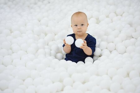 Cute child sits in dry pool of white balls and plays looks at camera.の写真素材