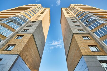 Two facades of symmetrical high brick residential buildings in city, against blue sky, view from below.の写真素材