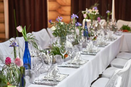 Beautiful table setting with crockery and fresh flowers on white table cloth before party, wedding reception or other festive event. Glassware and cutlery for catered dinner.の写真素材