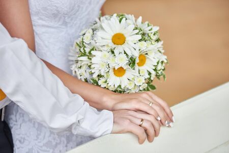 Hands together of bride and groom with wedding rings and bridal bouquet, closeup. Newlywed couple place their hands on banister.の写真素材