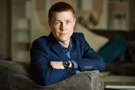 Portrait of a young man leaning his elbows on the back of a sofa, looking at the camera.の写真素材