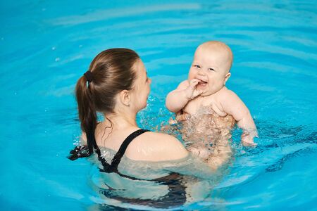 Mother teaching happy little baby to swim in water pool. Swimming lessons for children. Healthy Family Life.の写真素材