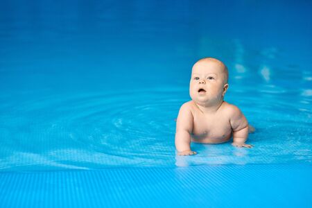 Little baby boy lying in blue swimming pool in water. Concept active lifestyle of child.の写真素材