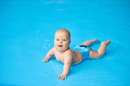 Portrait happy, smiling little baby boy lying in blue swimming pool in water. Concept active lifestyle of child. Kid looks at the camera.の写真素材