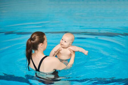 Mother teaching happy little baby to swim in water pool. Swimming lessons for children. Healthy Family Life.の写真素材