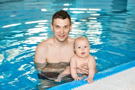 Happy Father and little baby boy in swimming pool look in the camera. Active family spending leisure.の写真素材