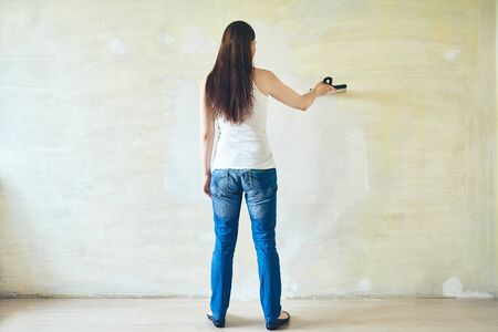 Woman plastering the walls with finishing putty in the room with putty knife or spatula. Repair work, decoration building concept, construction.の写真素材