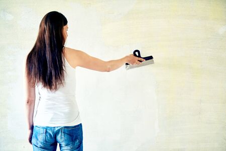 Woman plastering the walls with finishing putty in the room with putty knife or spatula. Repair work, decoration building concept, construction.の写真素材