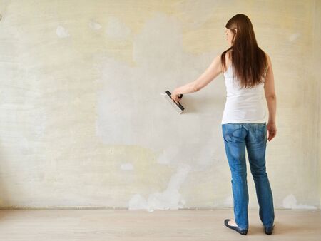 Woman plastering the walls with finishing putty in the room with putty knife or spatula. Repair work, decoration building concept, construction.の写真素材
