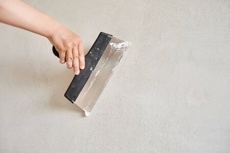 Spatula with putty in hand against a light wall. Worker puts of plaster. Repair work. Plastering wall.の写真素材
