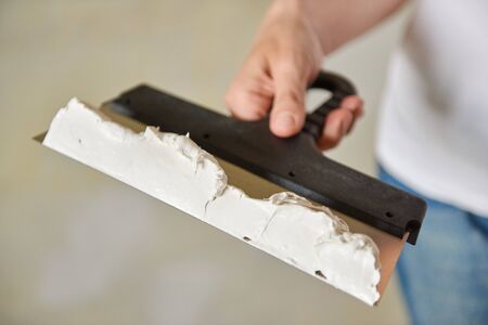 Spatula with white putty in hand. Repair work. Plastering wall. Close up.の写真素材