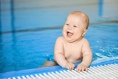 Portrait of happy, smiling little baby boy on edge of swimming pool in water. Concept active lifestyle of child.の写真素材